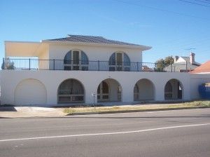 Two-story beige house with arched windows and balcony beside a street under a clear blue sky