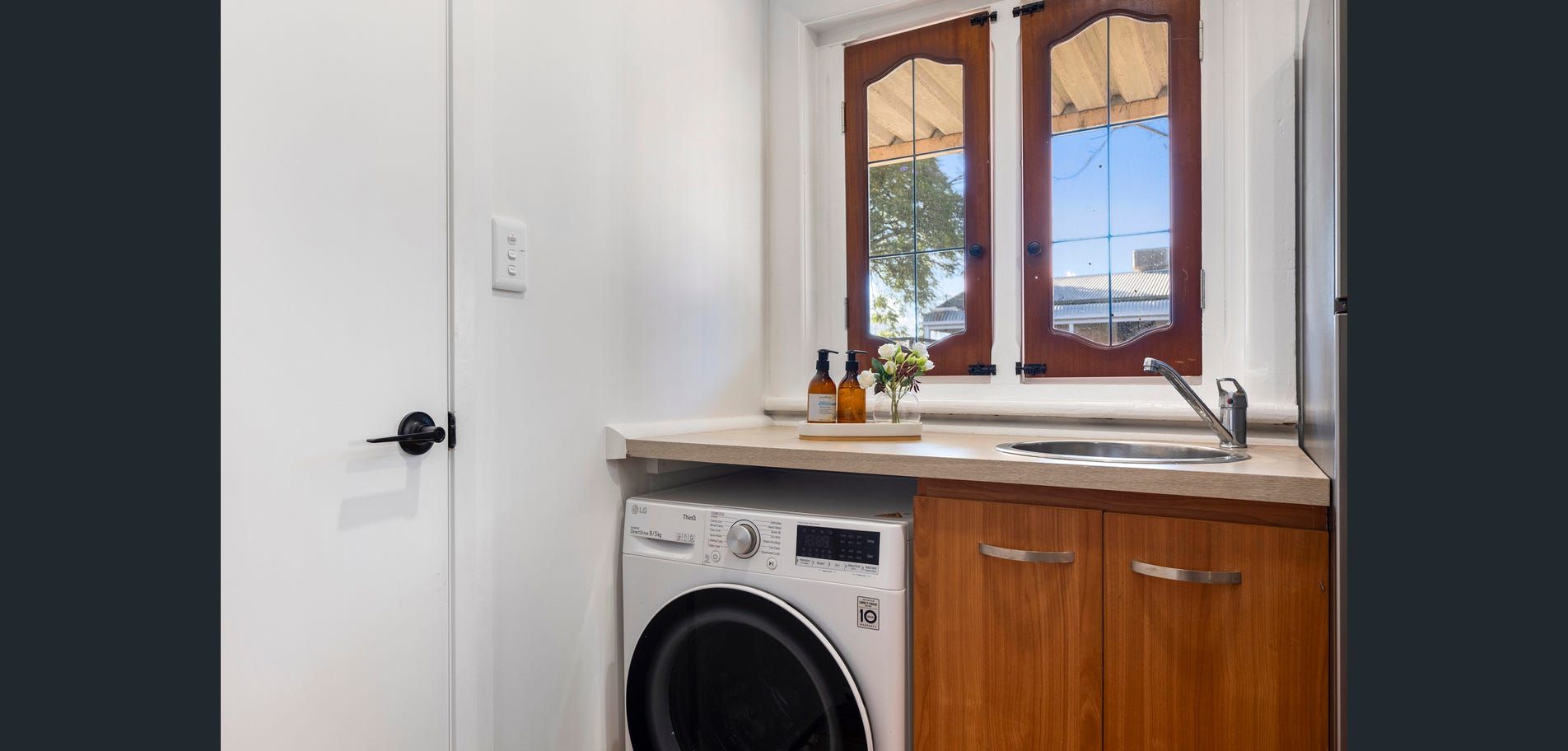 Bright laundry room with a front-load washer, wooden cabinets, and a window above the sink counter