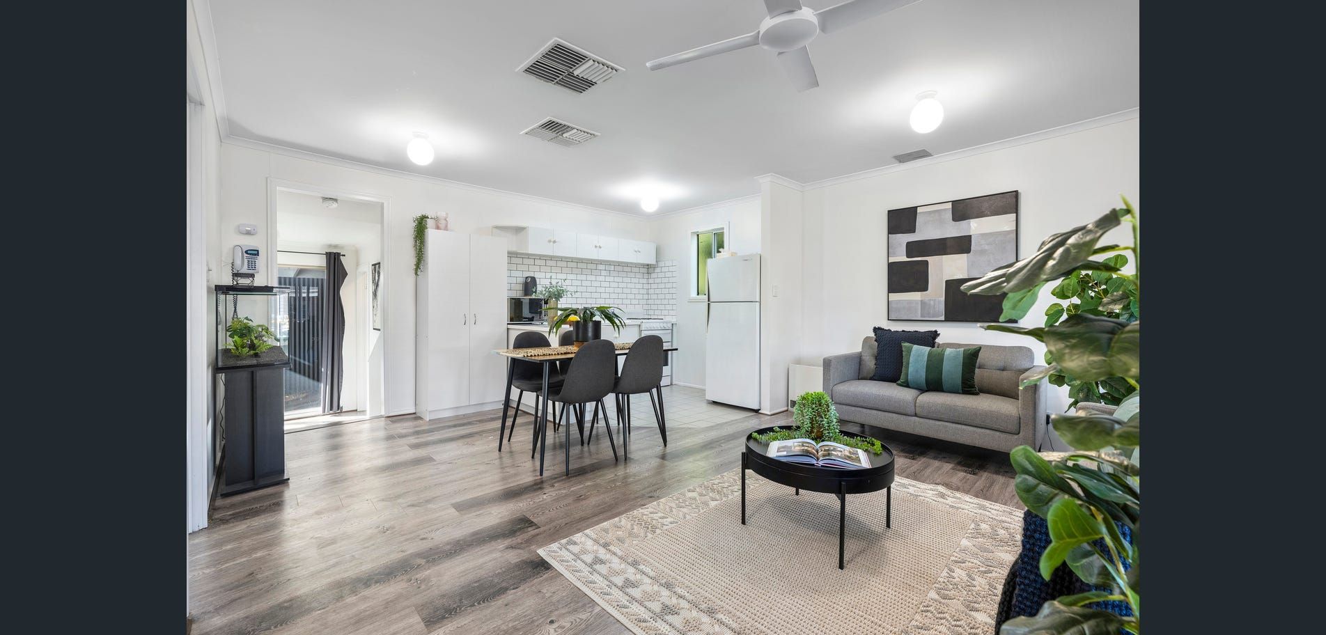 Bright modern open-plan living room with gray sofa, dining table, plants, and rug on wood flooring