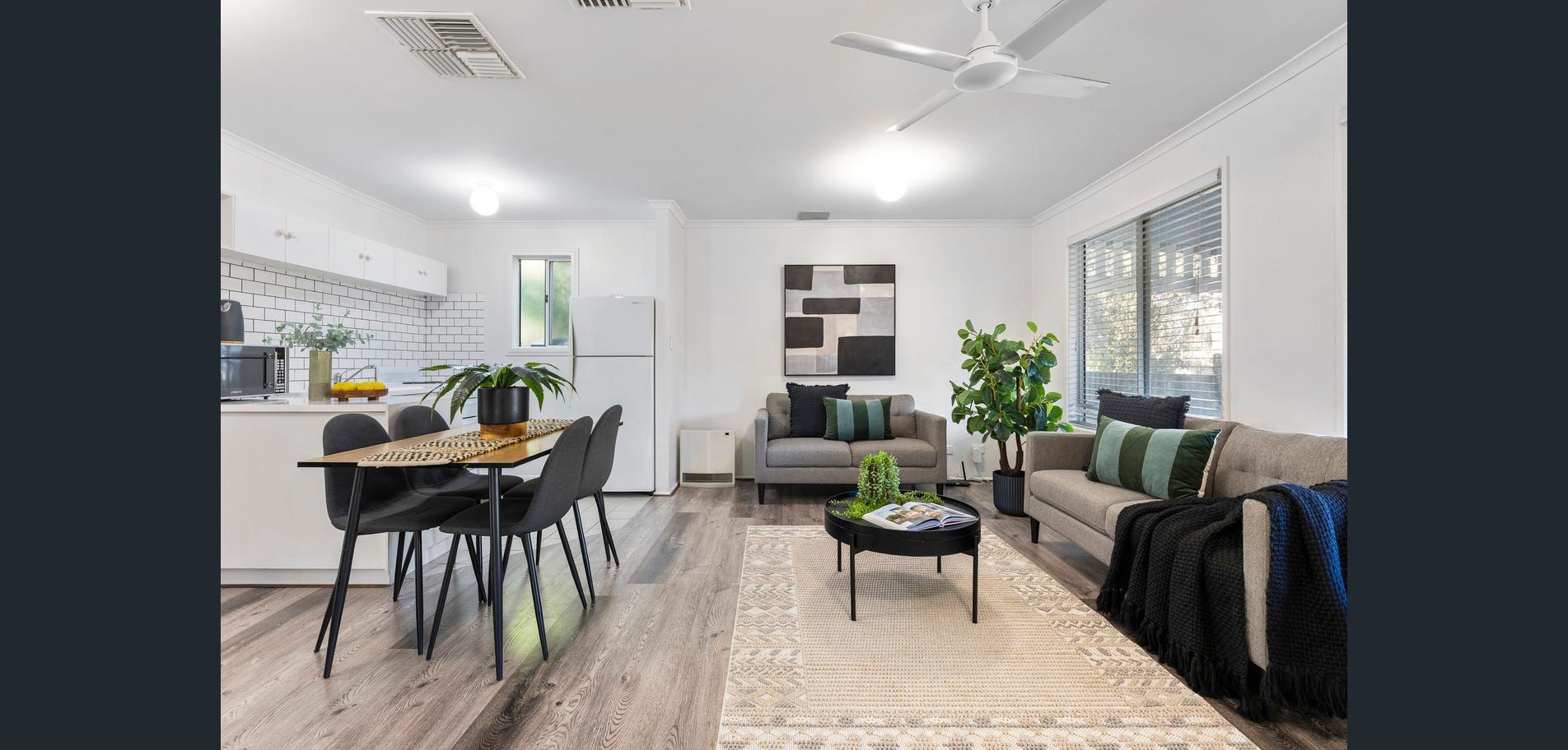 Bright open-plan living room and kitchen with gray sofas, dining table, and large windows