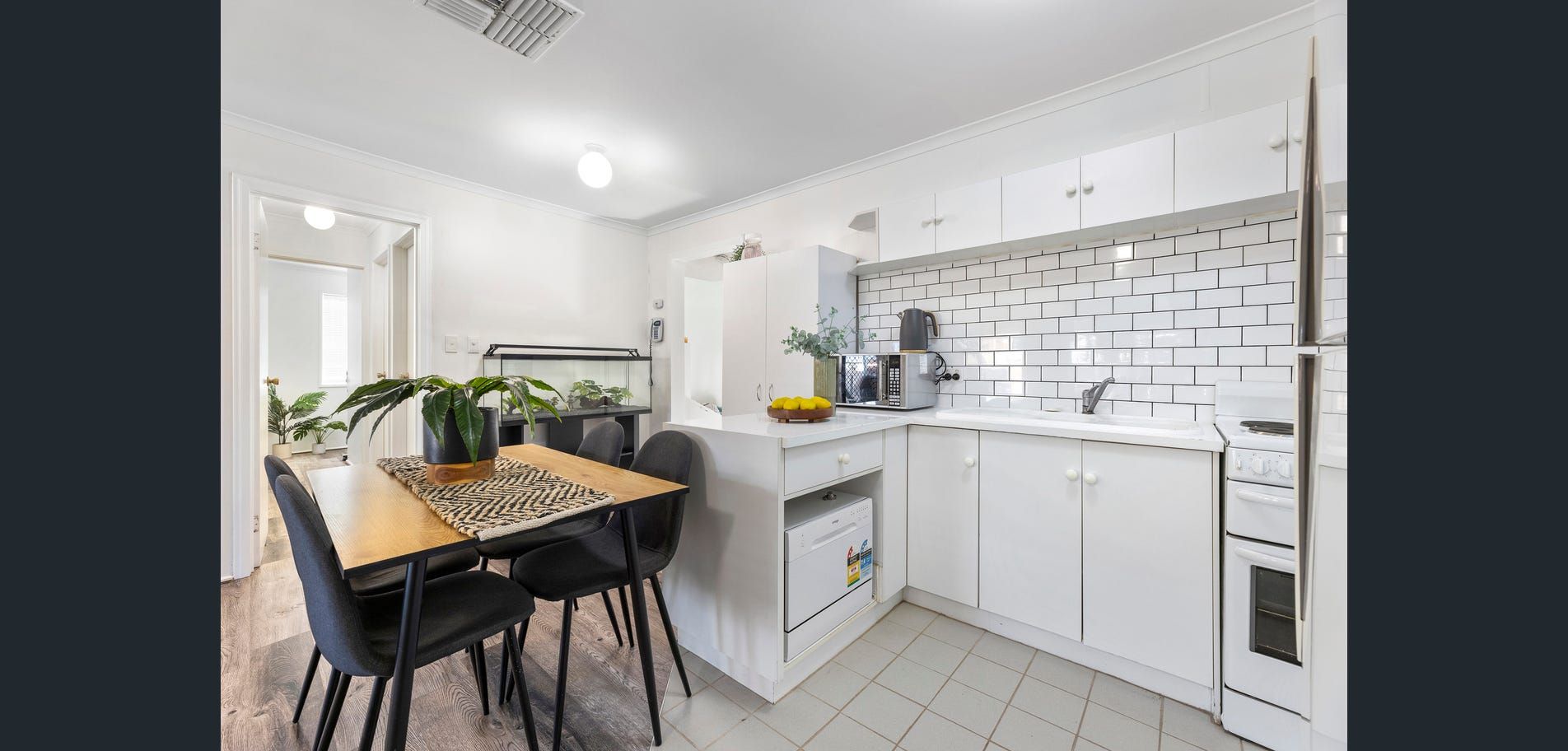 Bright white kitchen with black dining chairs, wooden table, and tiled backsplash