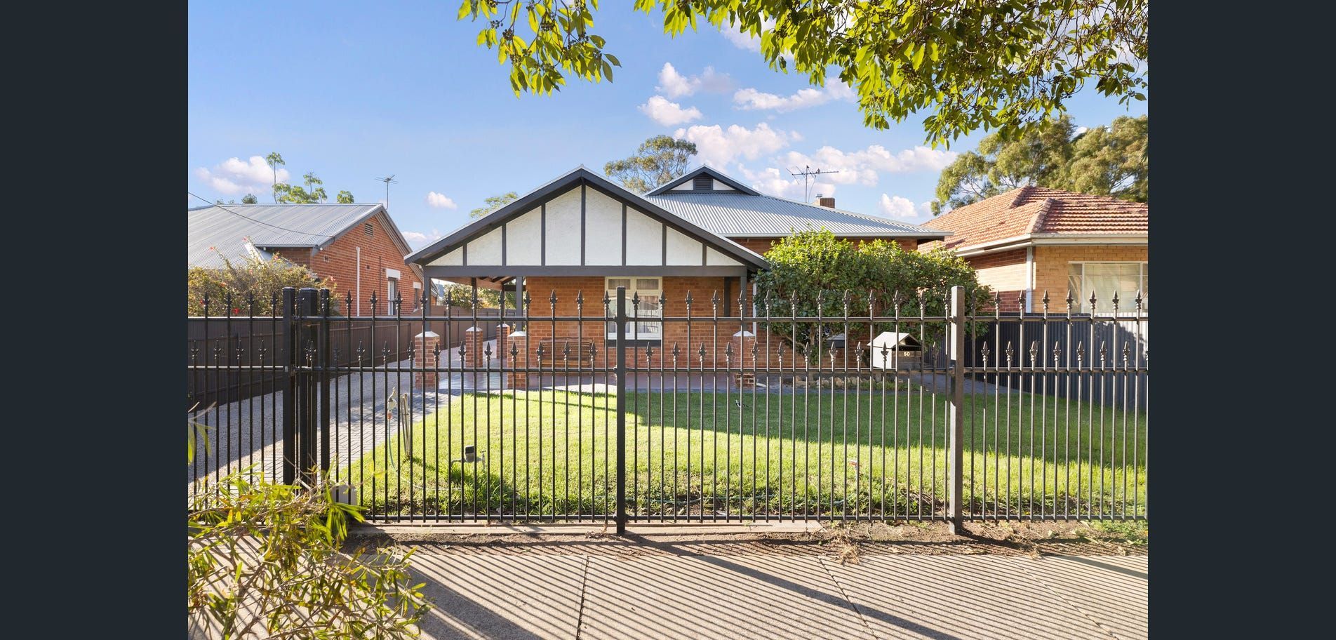 Suburban house with black metal fence, brick facade, and a front yard on a sunny day
