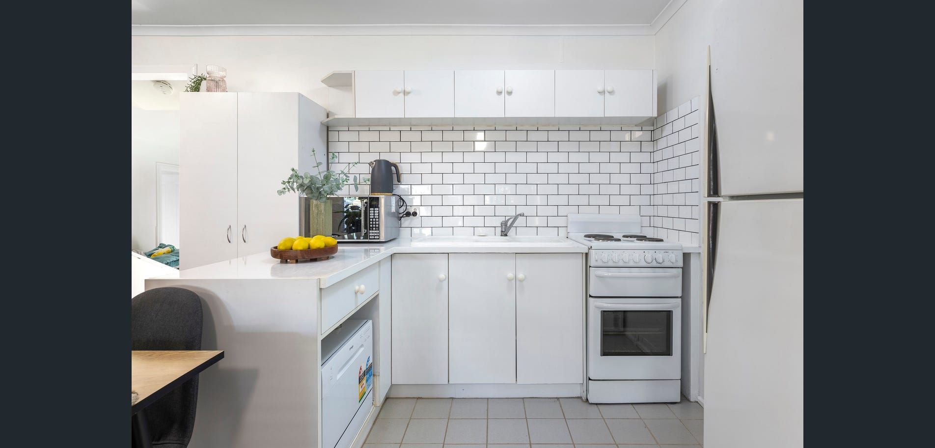 Bright white modern kitchen with subway tile, cabinets, stove, and fruit on the counter