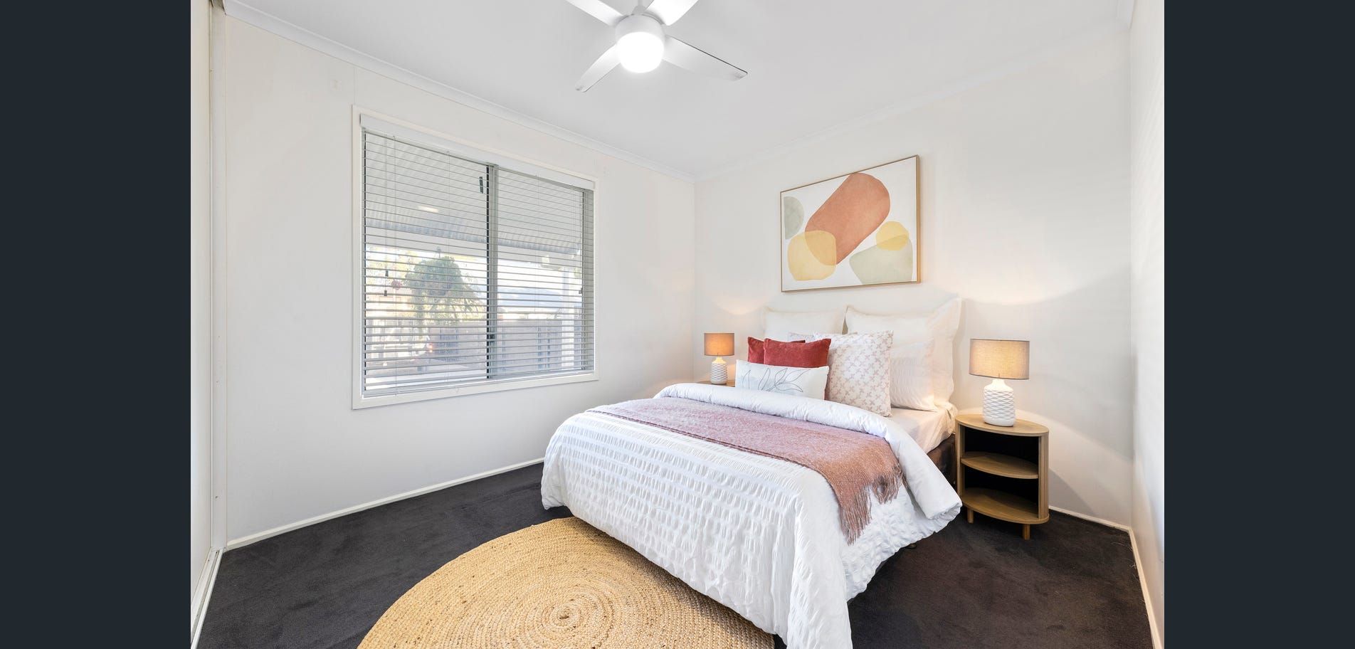 Bright white bedroom with a bed, bedside tables, window blinds, and abstract wall art