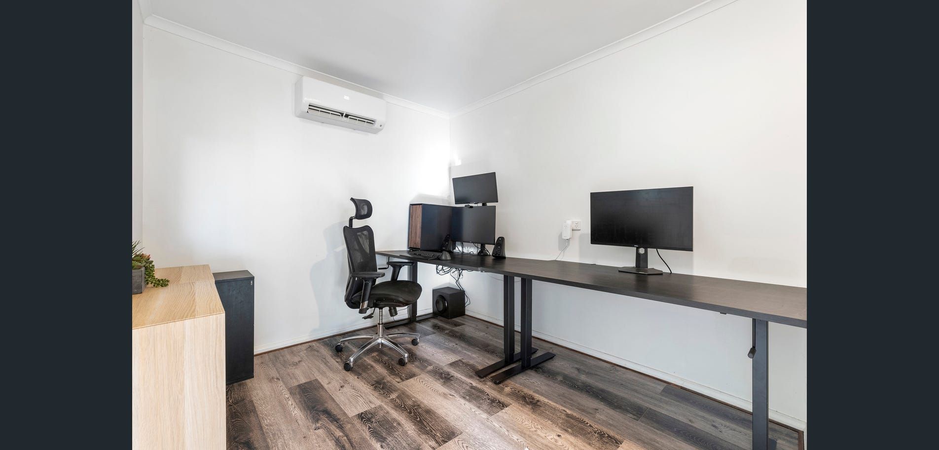 Minimalist home office with two desks, monitors, chair, and wall-mounted air conditioner