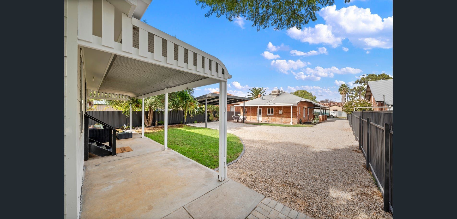 Covered carport beside a gravel driveway and single-story house under a bright blue sky