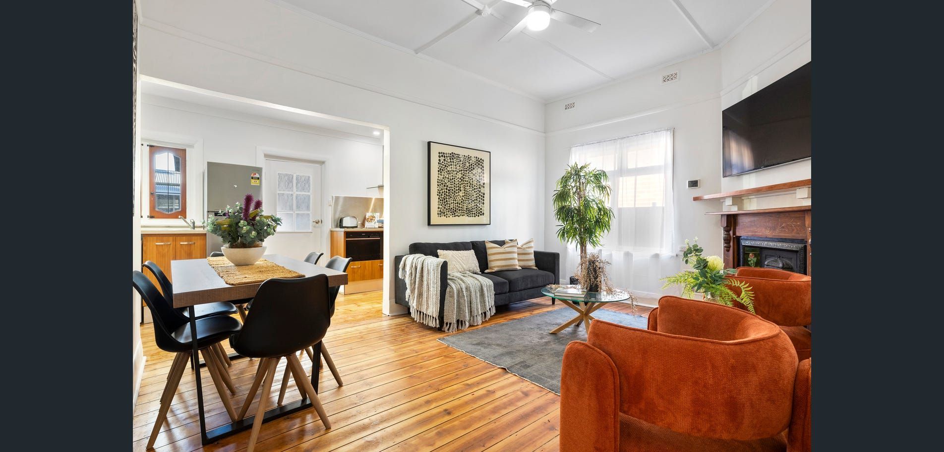 Bright living room with wood floors, orange chair, black dining chairs, bookshelves, and large windows