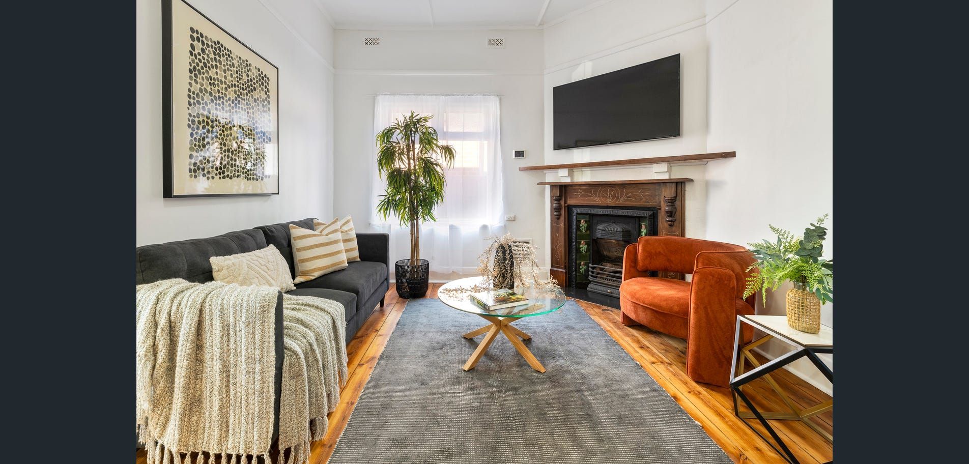 Bright living room with a gray sofa, orange chair, fireplace, coffee table, and large wall art