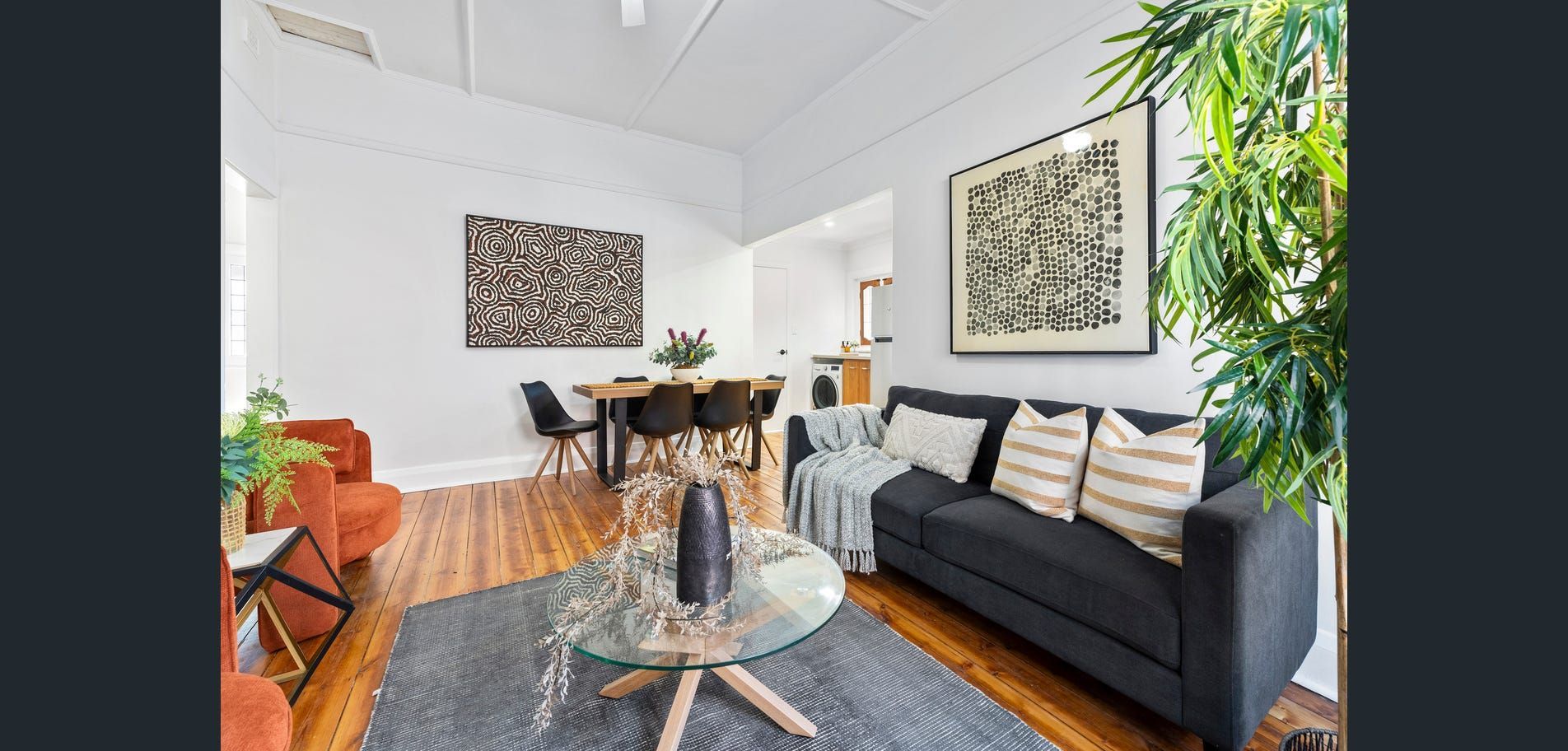 Bright modern living room with black sofa, orange chair, glass coffee table, and indoor plants