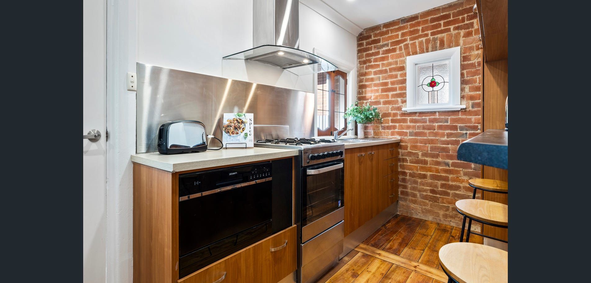 Compact kitchen with stainless steel appliances, brick wall, wood floors, and a small dining area