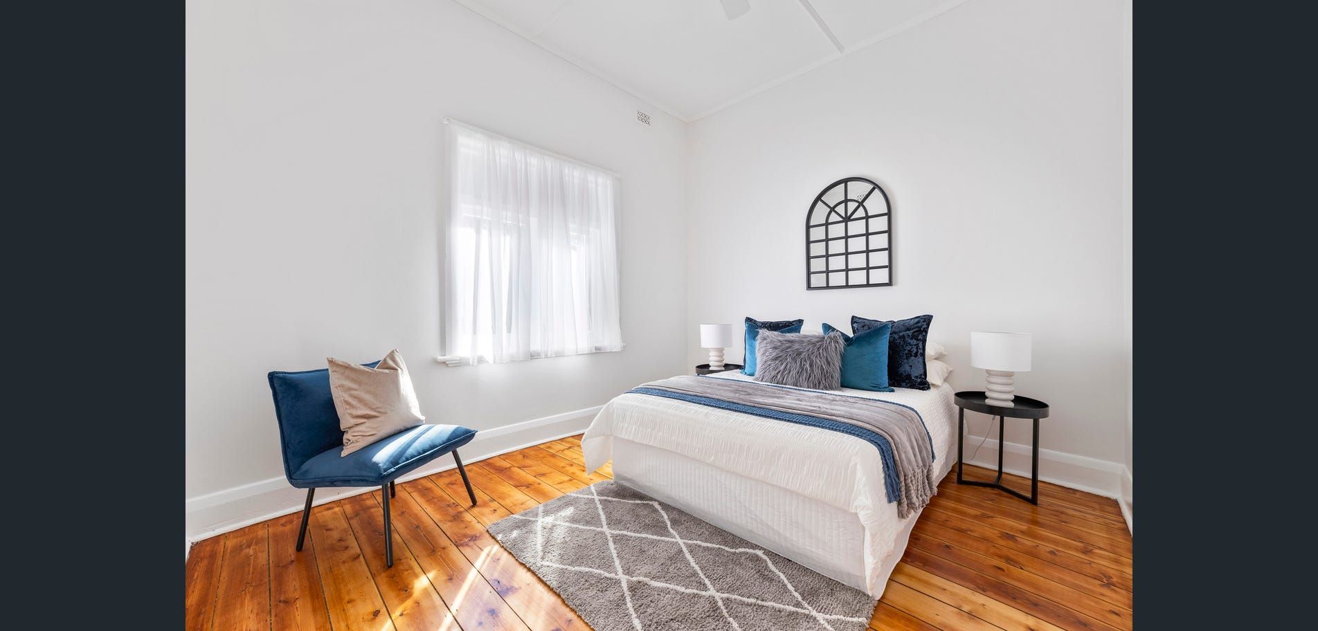 Bright bedroom with white walls, wooden floor, bed, blue chair, and sunlight through a window