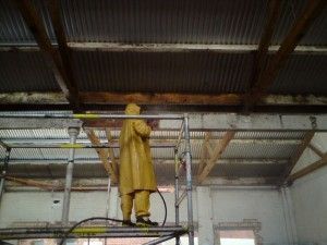 Worker in yellow protective gear on scaffolding inside an industrial building.
