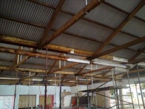 Interior of a bare warehouse with corrugated metal roof, exposed beams, and columns under construction