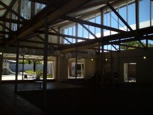 Dim industrial interior with exposed wooden beams, large windows, and bright daylight outside.