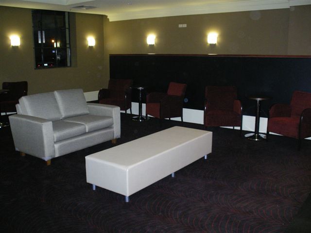 Dim lounge with white sofa, long ottoman, and red chairs against a dark wall
