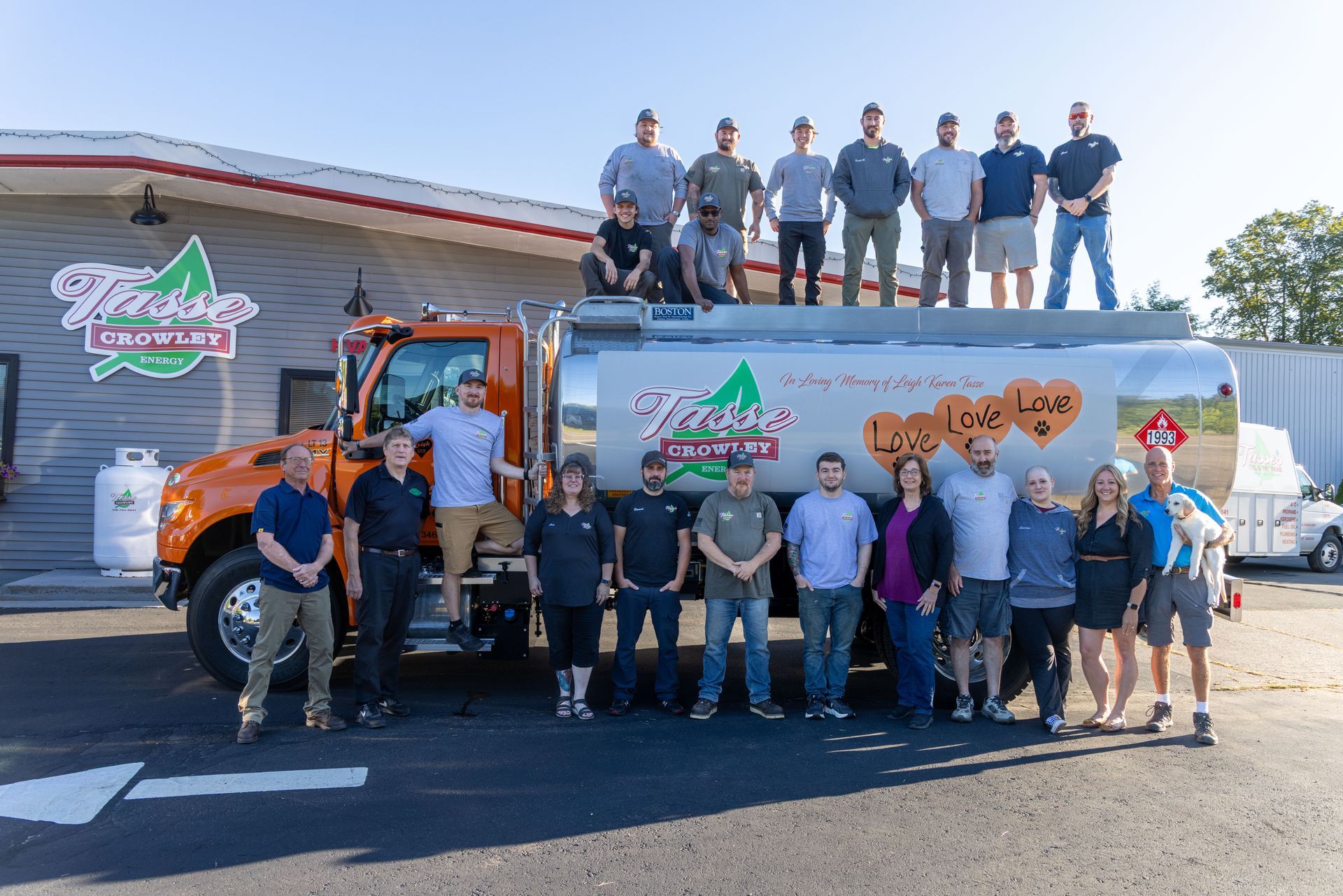 Group of people pose with a tanker truck in front of a building with a company sign.