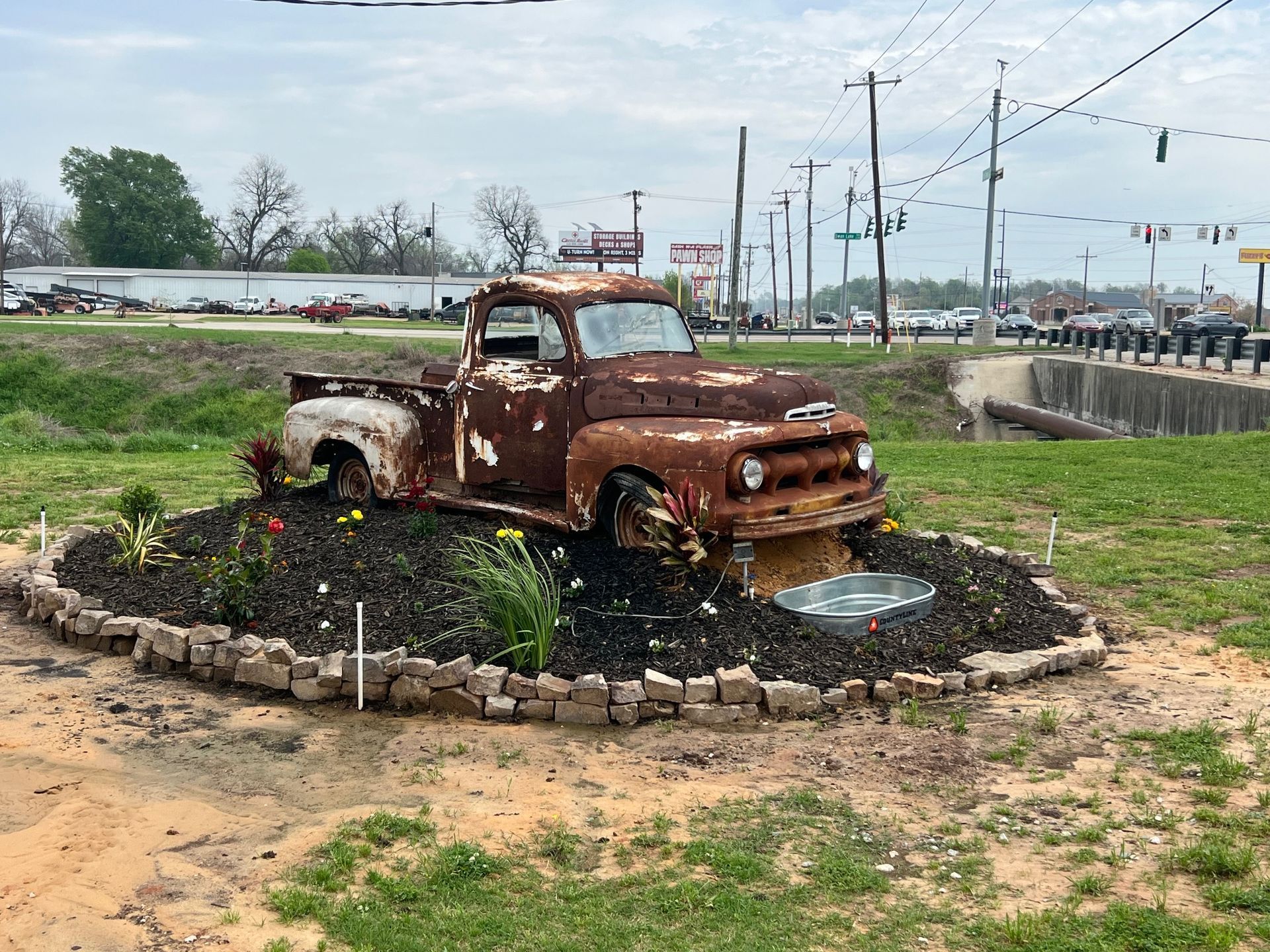 An old rusty truck is sitting in the middle of a garden.