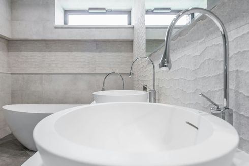 Modern kitchen sink with chrome faucet, white countertop, and soap dispenser by a window