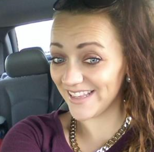 A woman wearing sunglasses and a necklace is smiling in a car.
