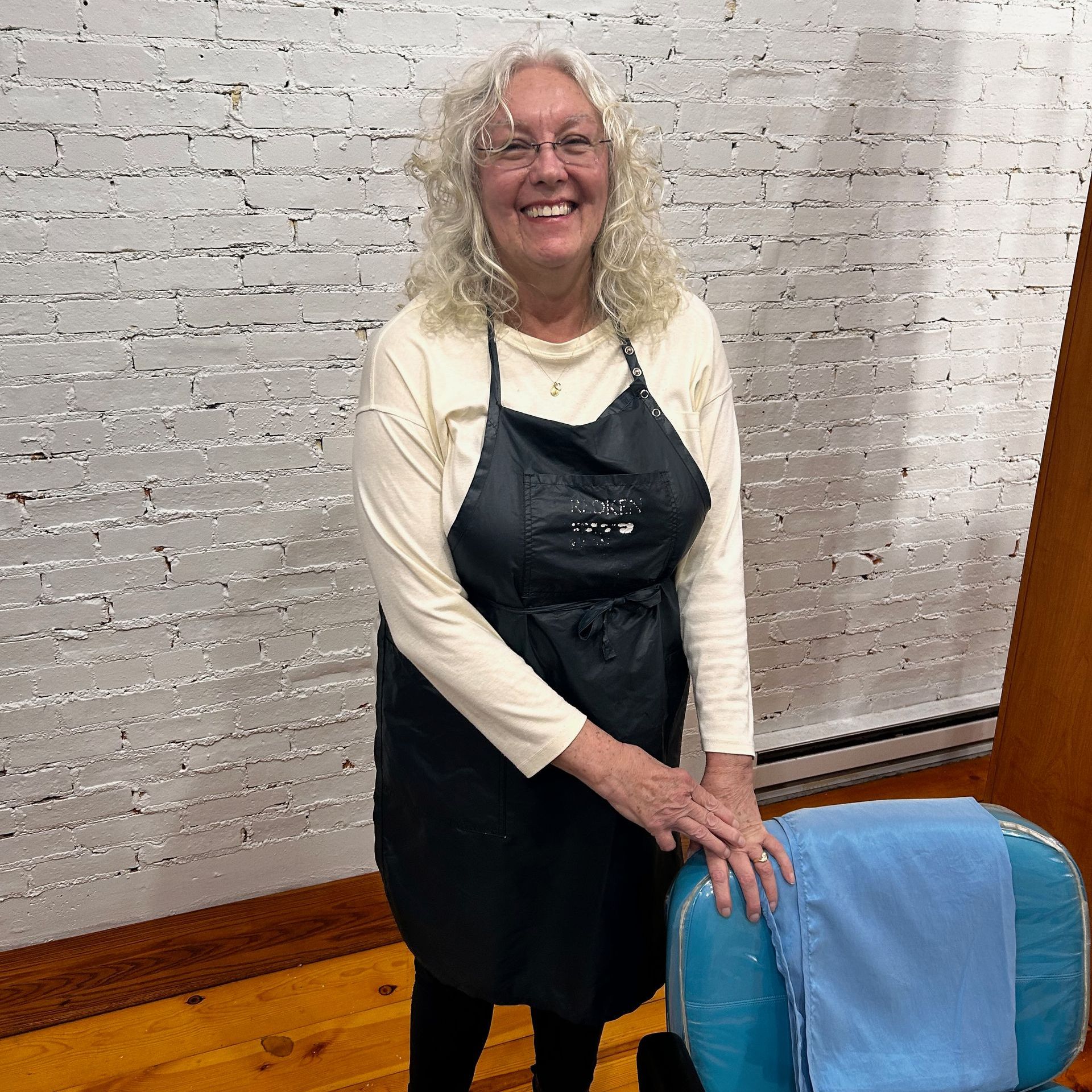 A woman in an apron is standing next to a blue chair.