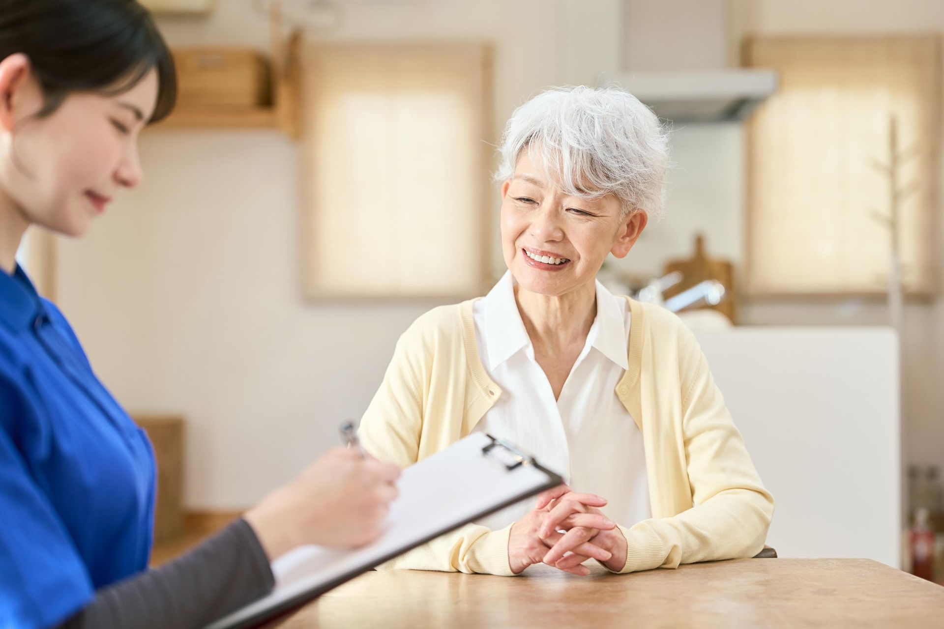Healthcare worker taking notes while smiling older patient speaks at a table