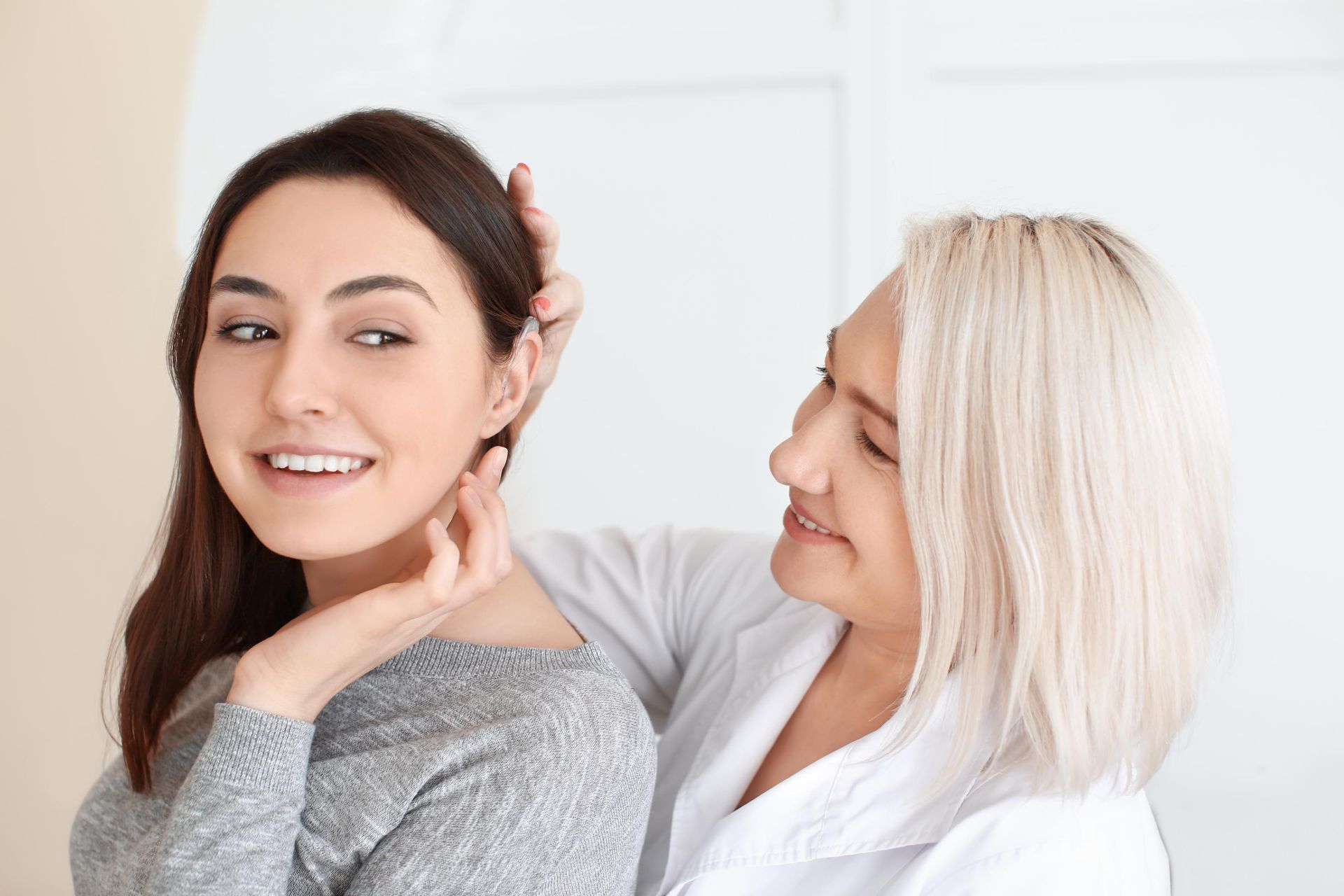 Two women smiling, with one adjusting the other's hair in a bright studio setting