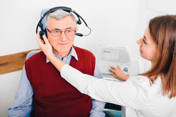 Woman checks elderly man's hearing aid at a clinic