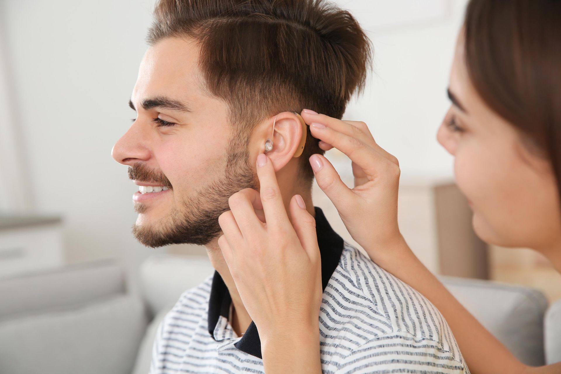 A person having a hearing check while another adjusts an ear device in a bright room