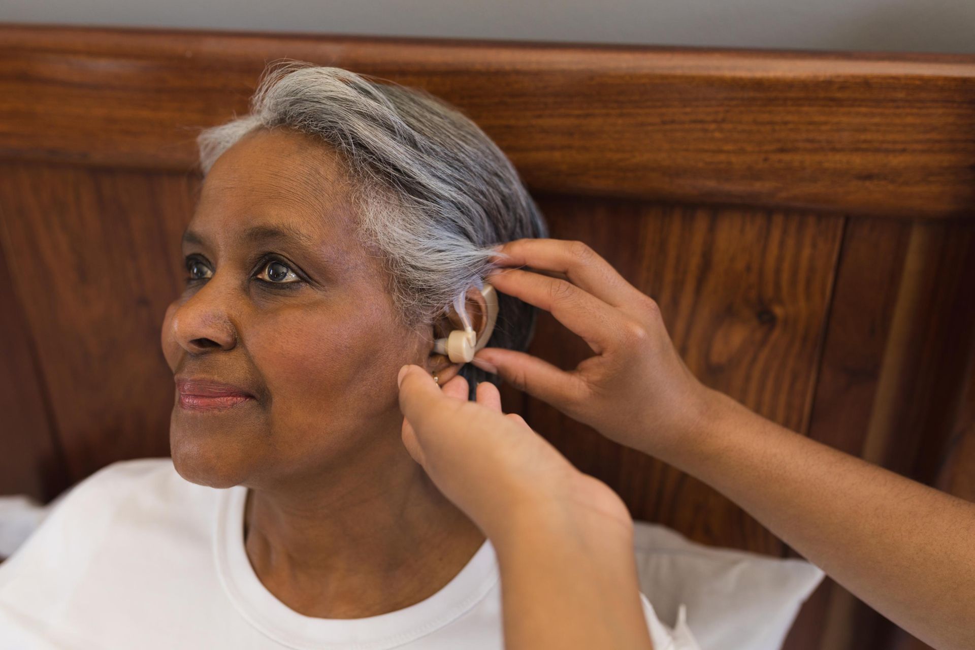 Person with gray hair receiving an ear piercing in a wooden-paneled room