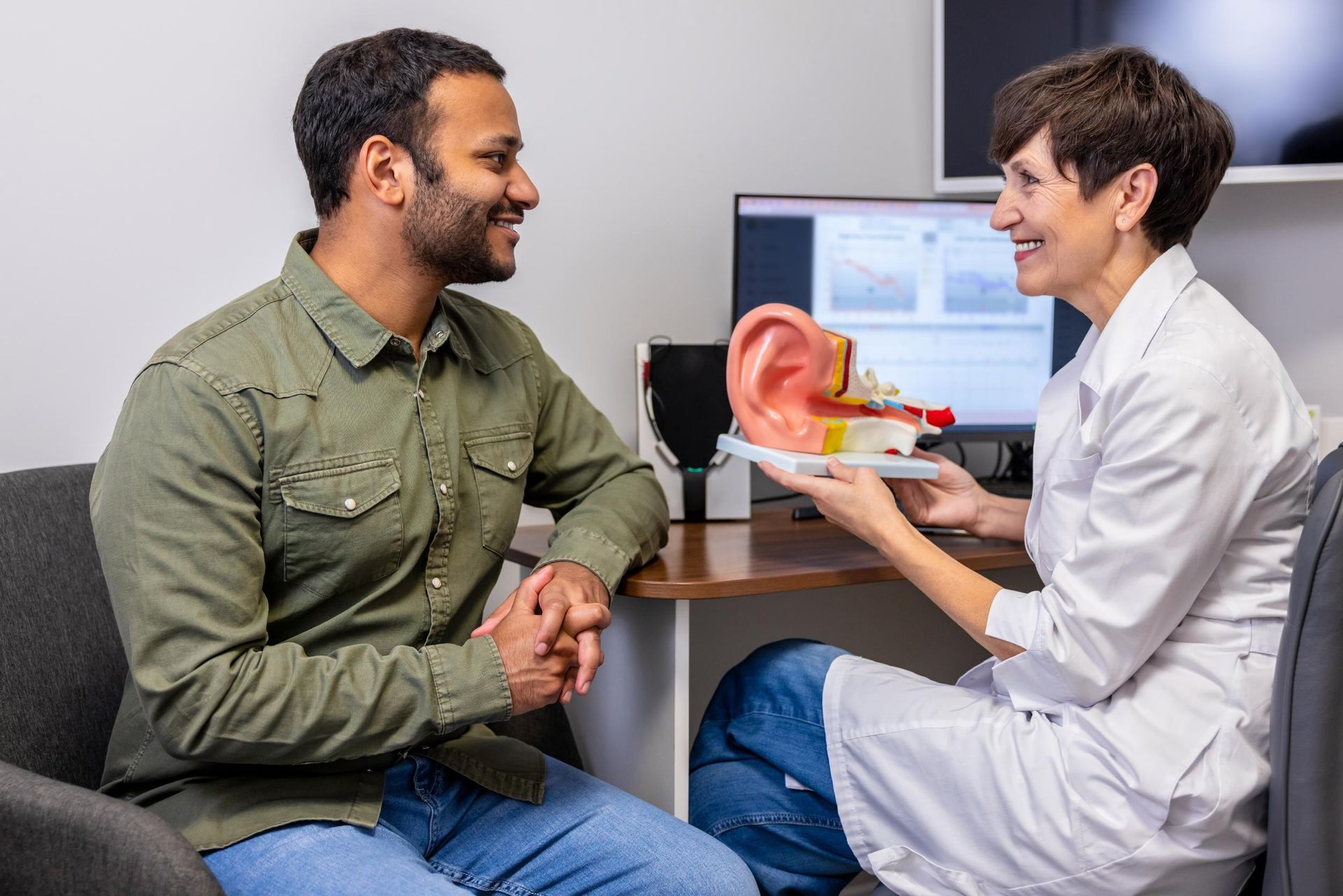 Doctor showing an ear model to a seated patient in a clinic office