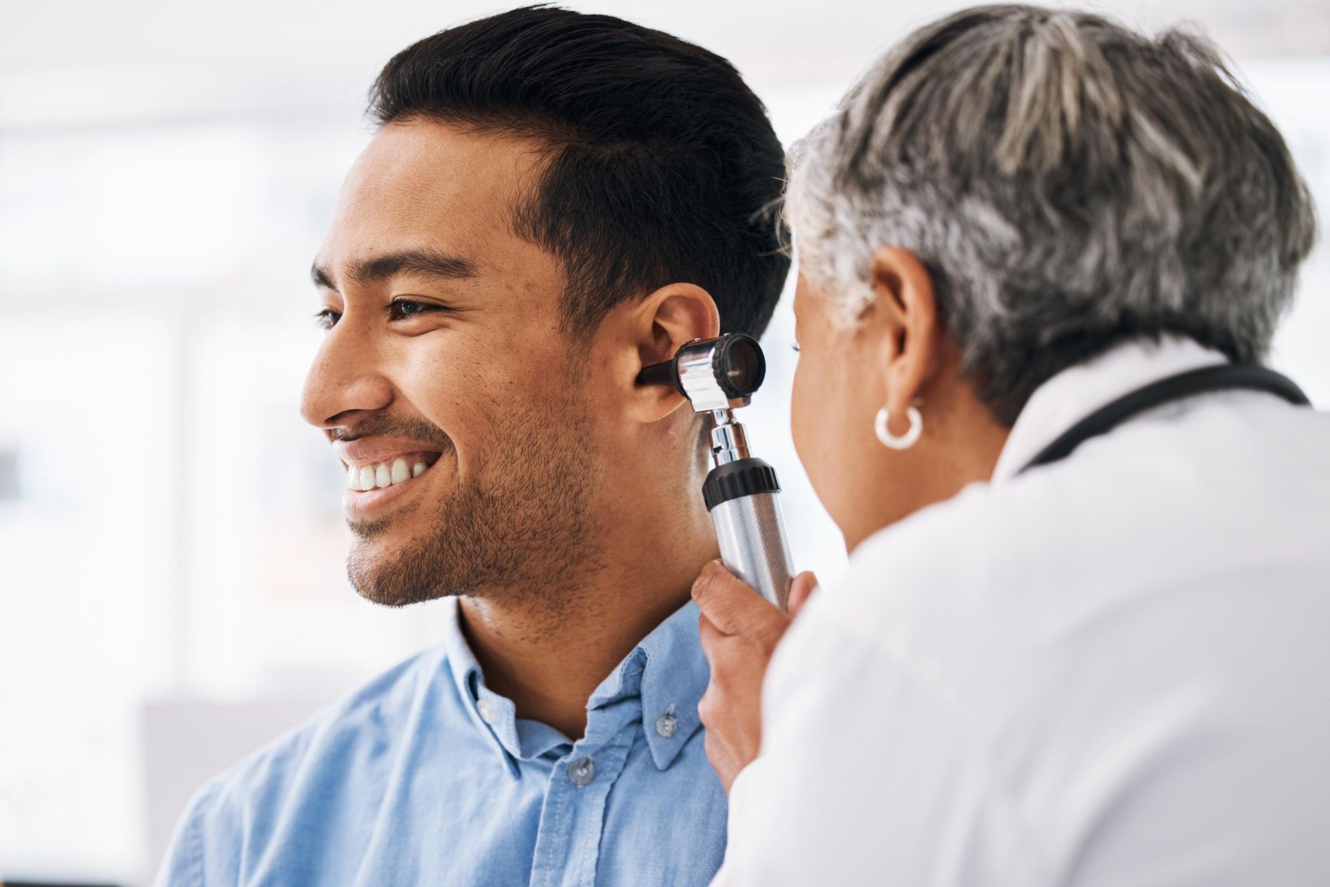 Doctor examining a smiling patient's ear with an otoscope in a bright clinic