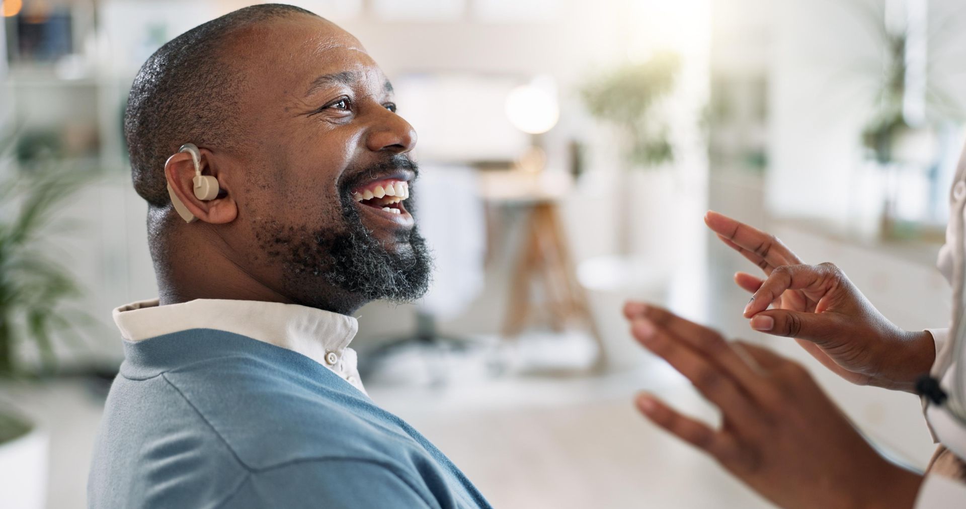 Smiling man wearing a hearing aid talking with someone in a bright office