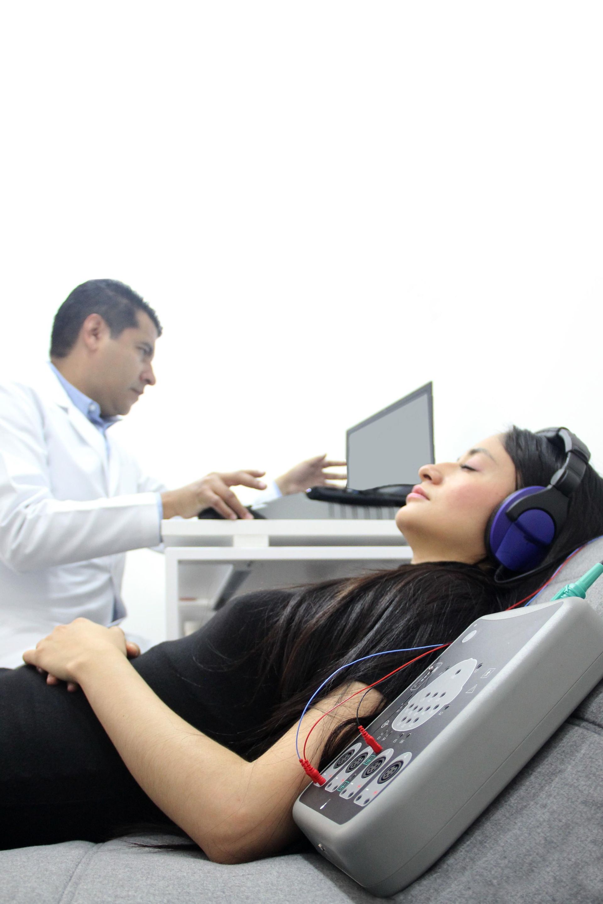 Woman reclining during a medical hearing test while a technician works at a computer nearby