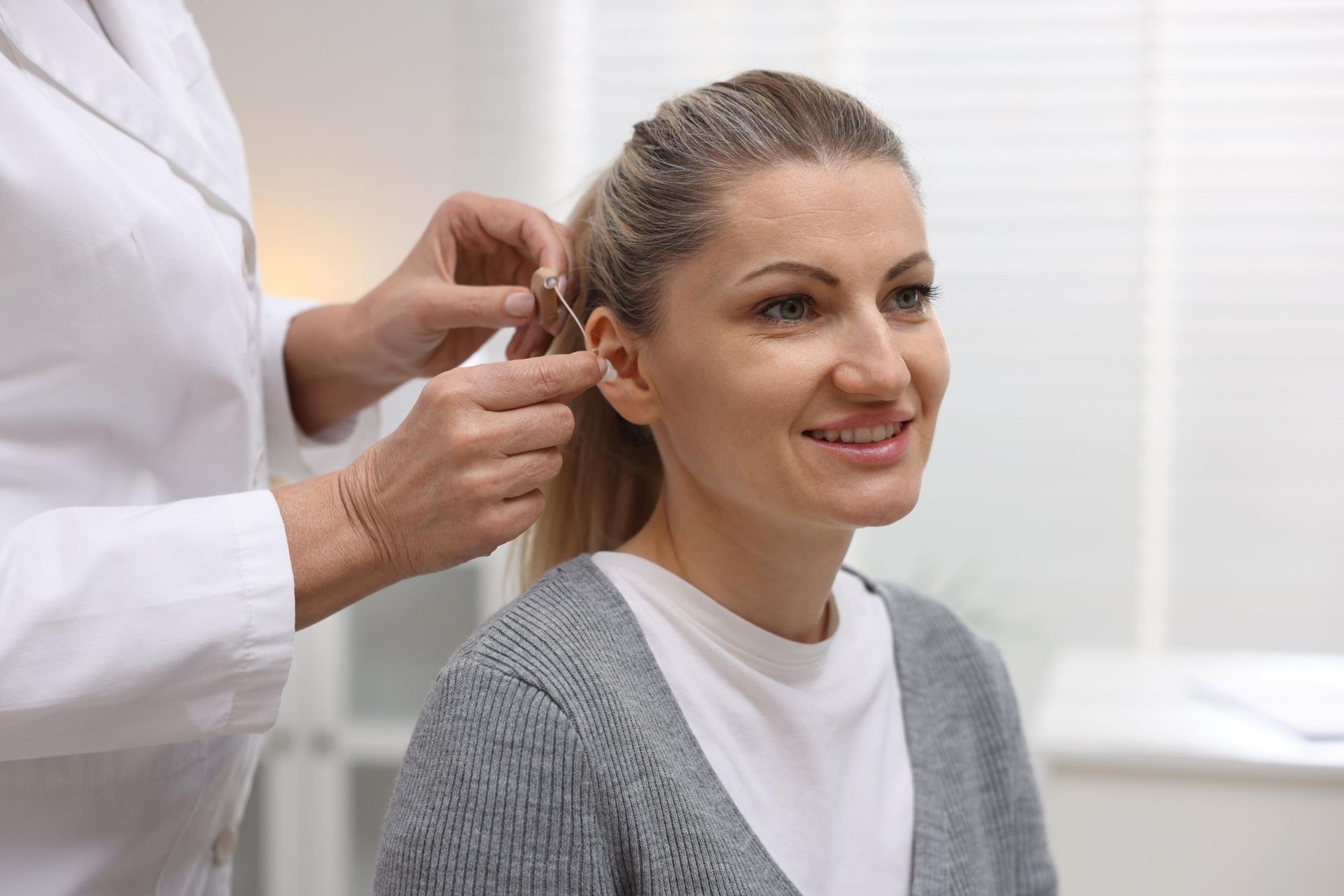 Person adjusting another person's ear with a medical instrument in a bright clinic setting
