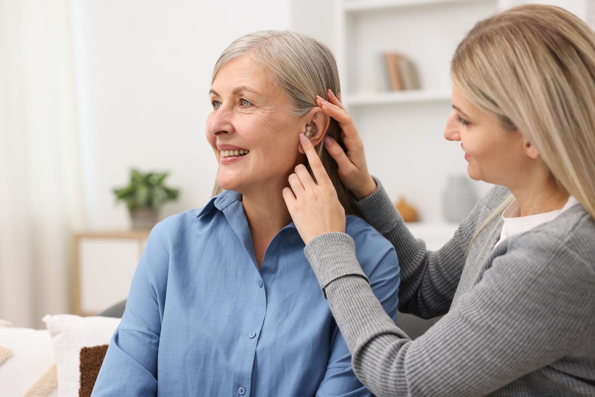 Woman examines an older woman’s ear in a bright living room