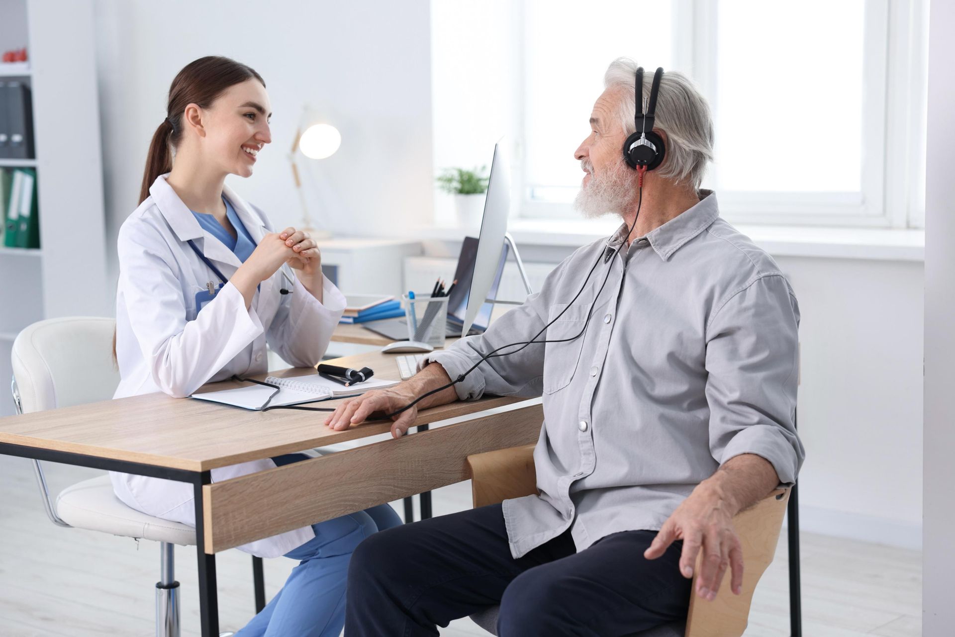 Woman and elderly man in a bright office, talking across a desk with a headset on the man