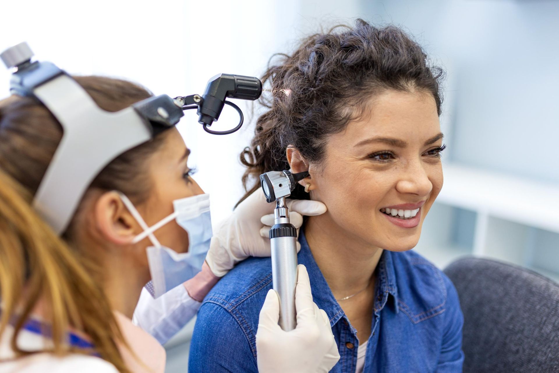 Dentist examining a smiling patient’s ear with medical tool in a clinic