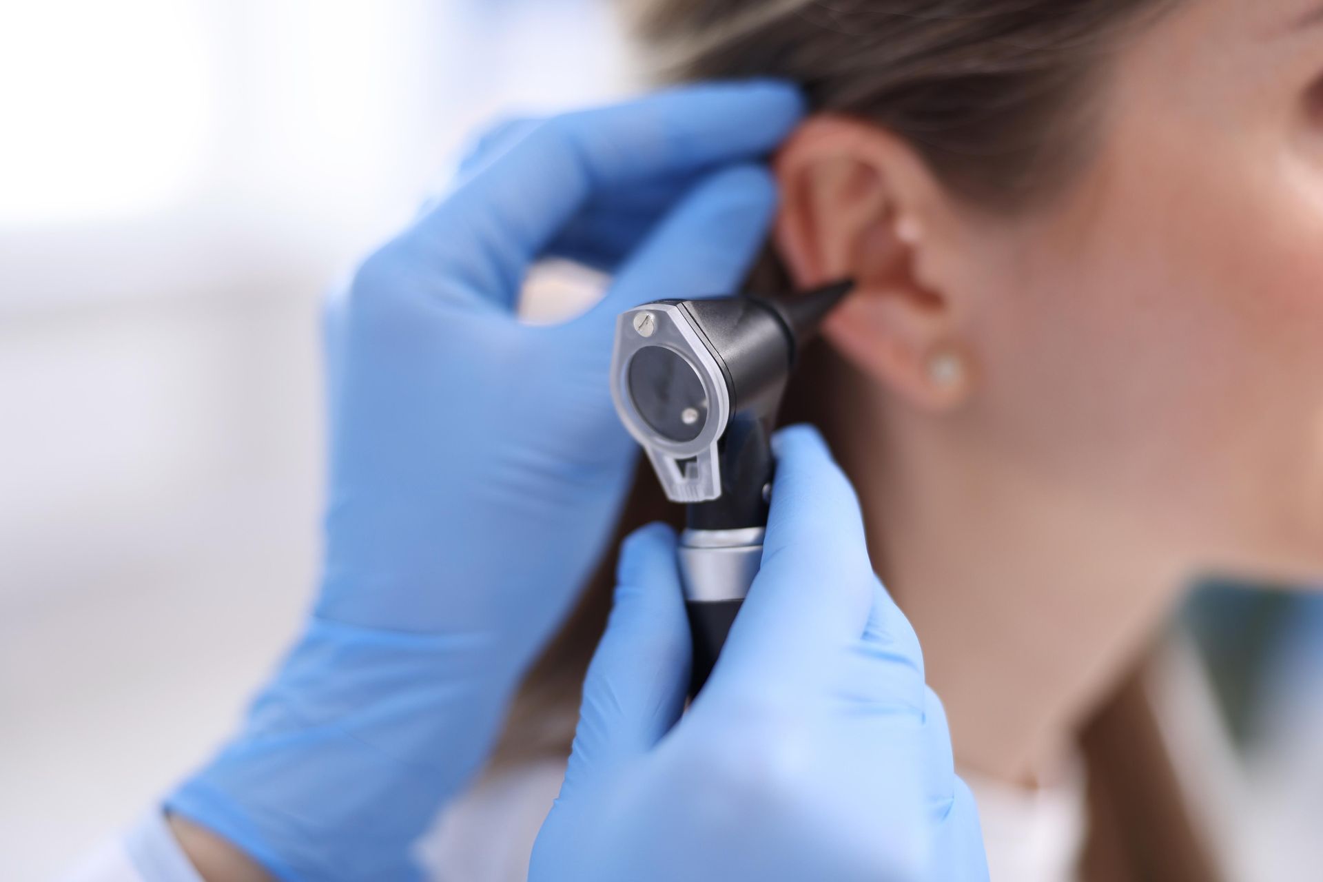 Gloved hands examining a woman’s ear with an otoscope