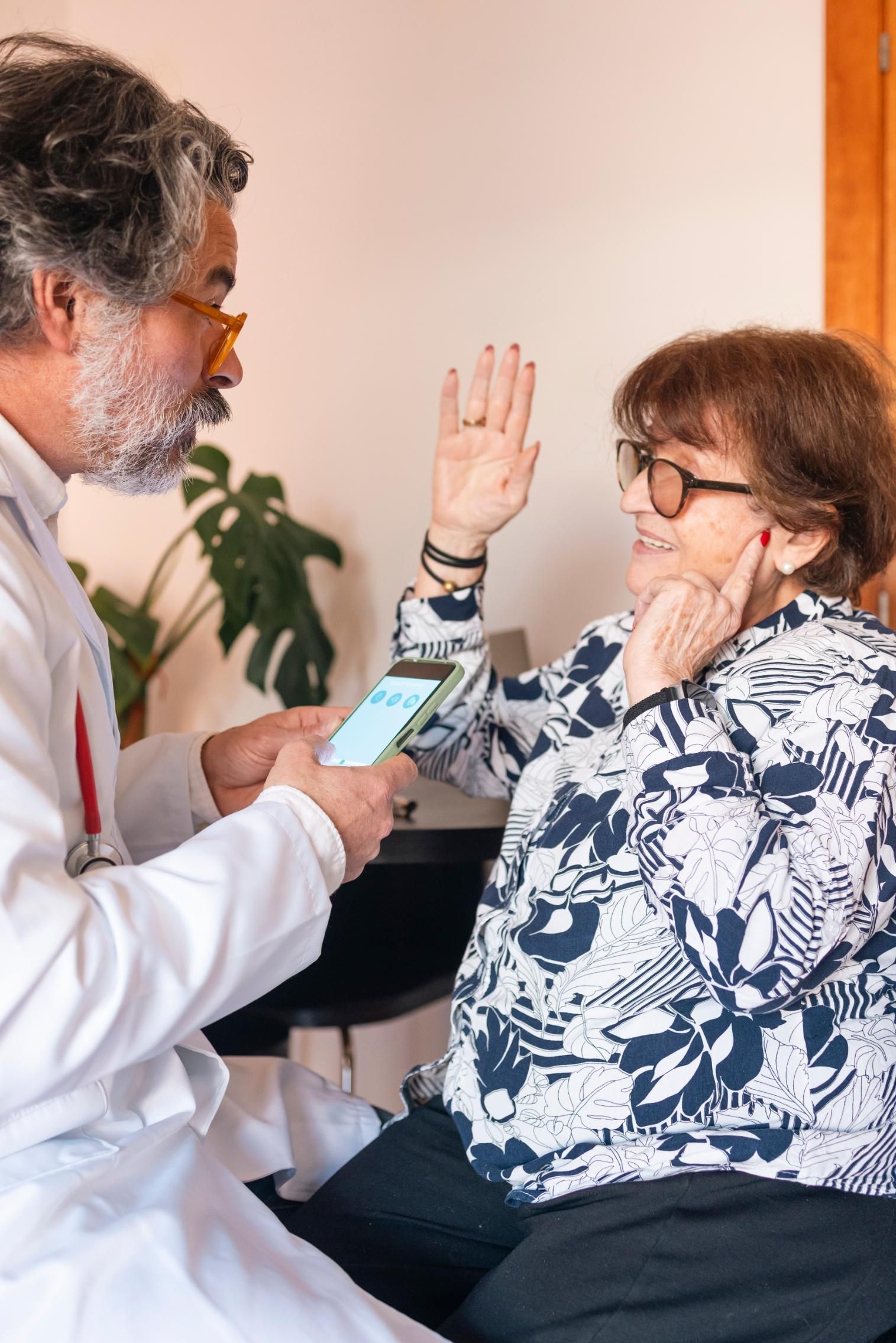 Doctor checking a seated patient’s blood pressure while she raises her hand and touches her face.