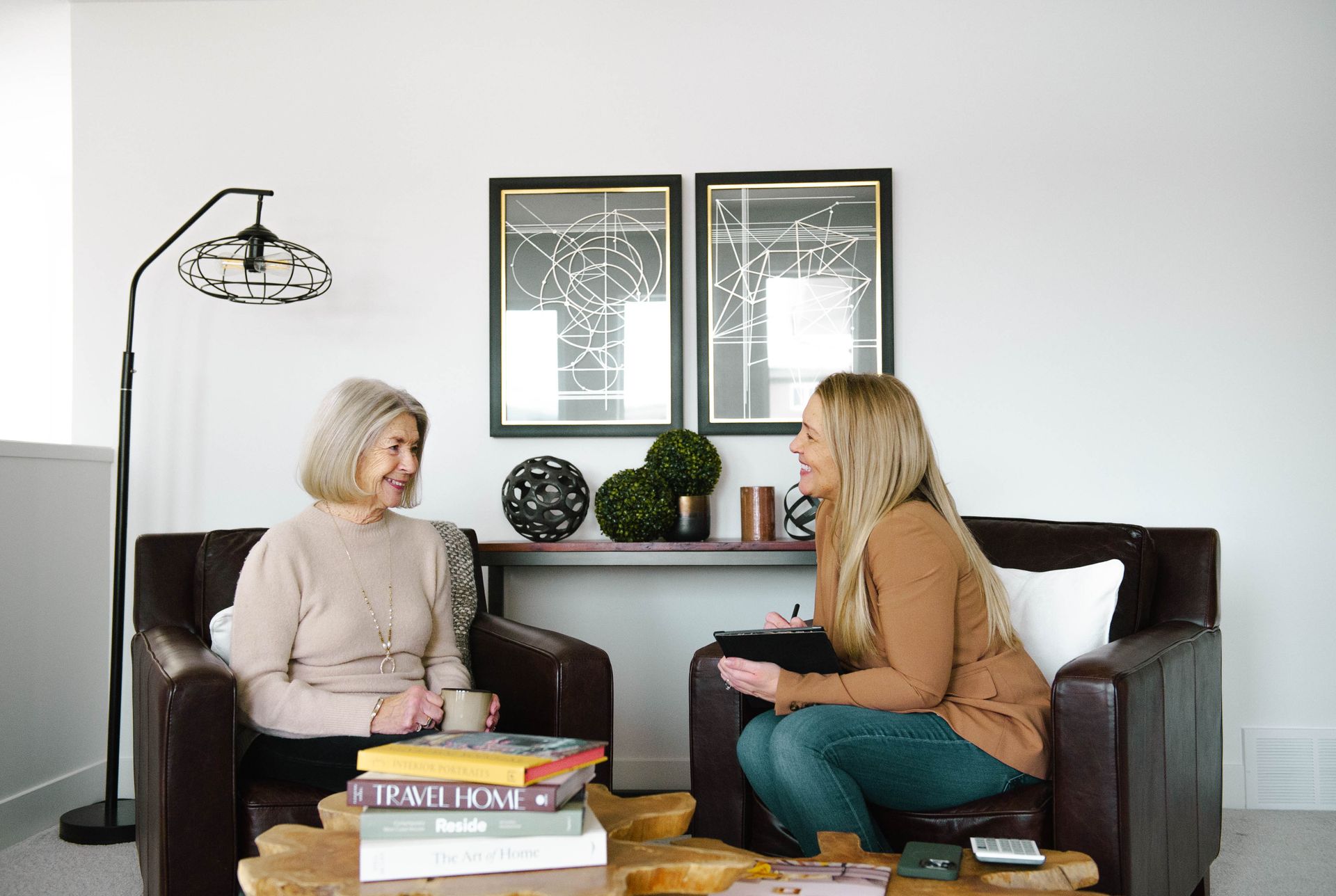 Two women are sitting in chairs talking to each other in a living room.