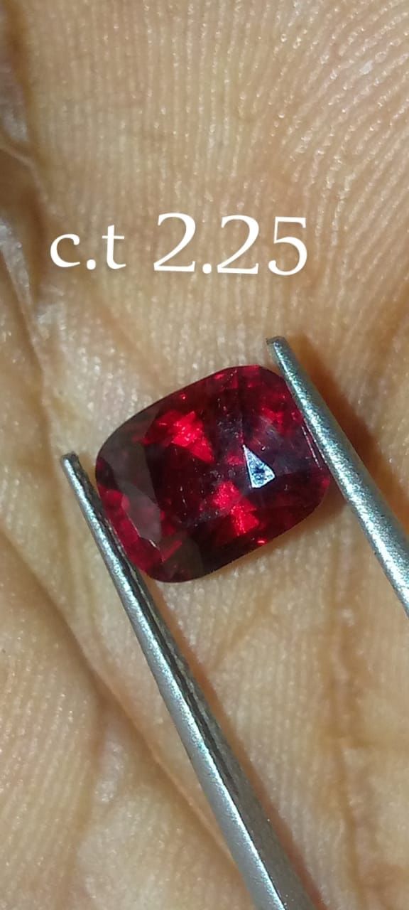Een klein rood edelsteentje, vastgehouden met een pincet op een vingertop, met het opschrift 