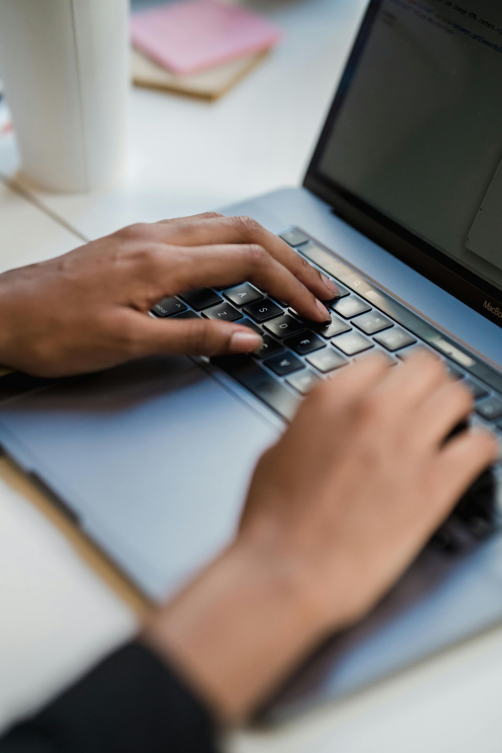 Hands typing on a laptop keyboard at a desk.