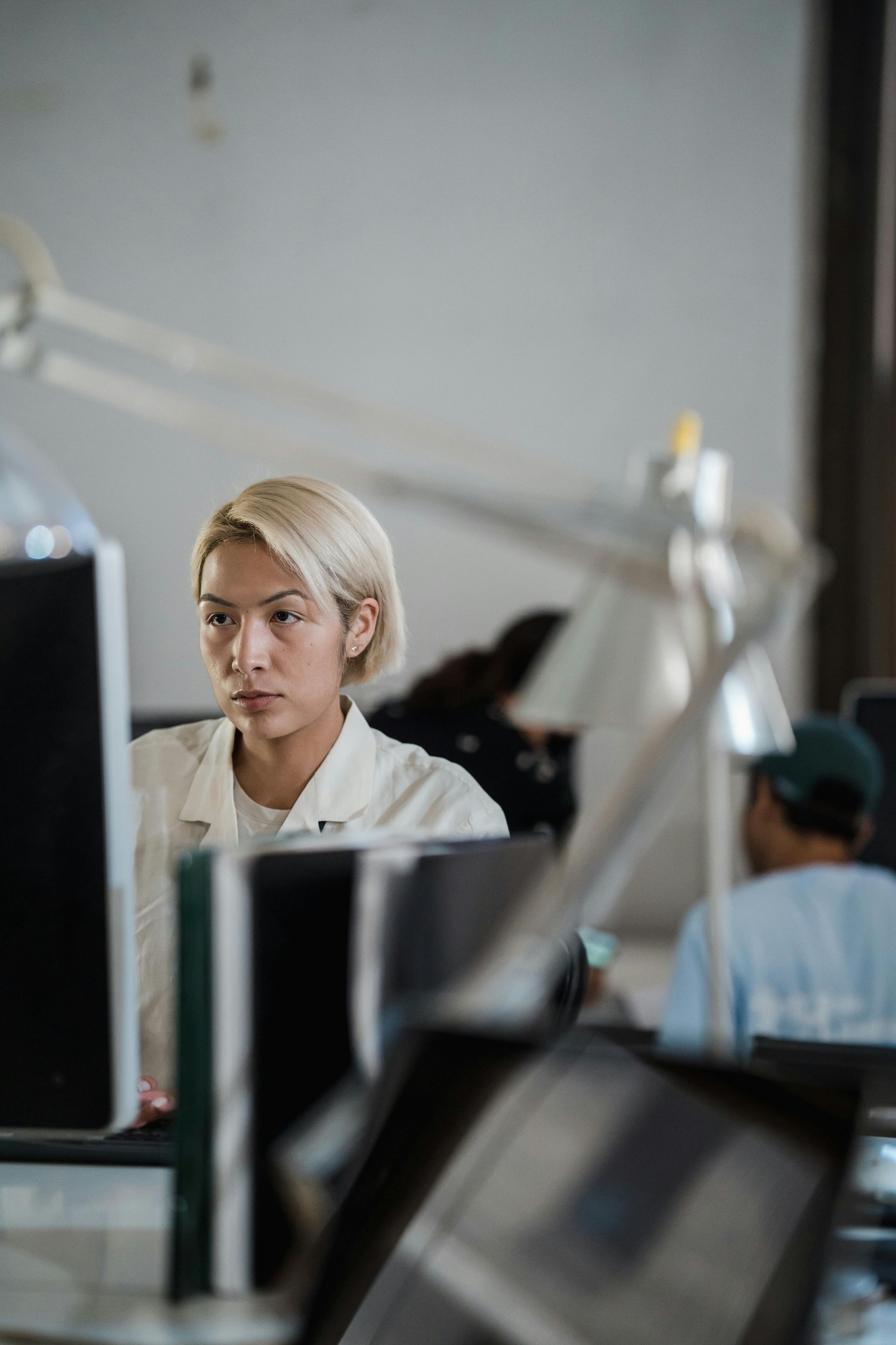 Person in a white shirt working at a desk in an office, with computer monitors in the foreground.