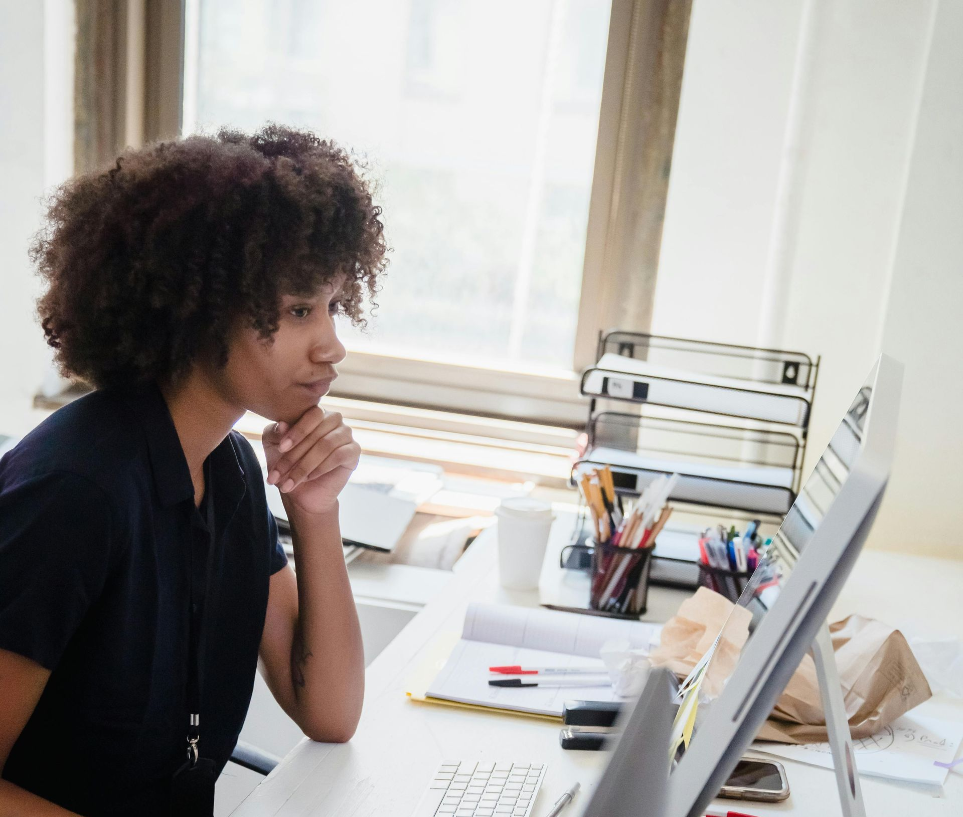 Person sitting at a desk, thinking while looking at a computer monitor in a bright office.