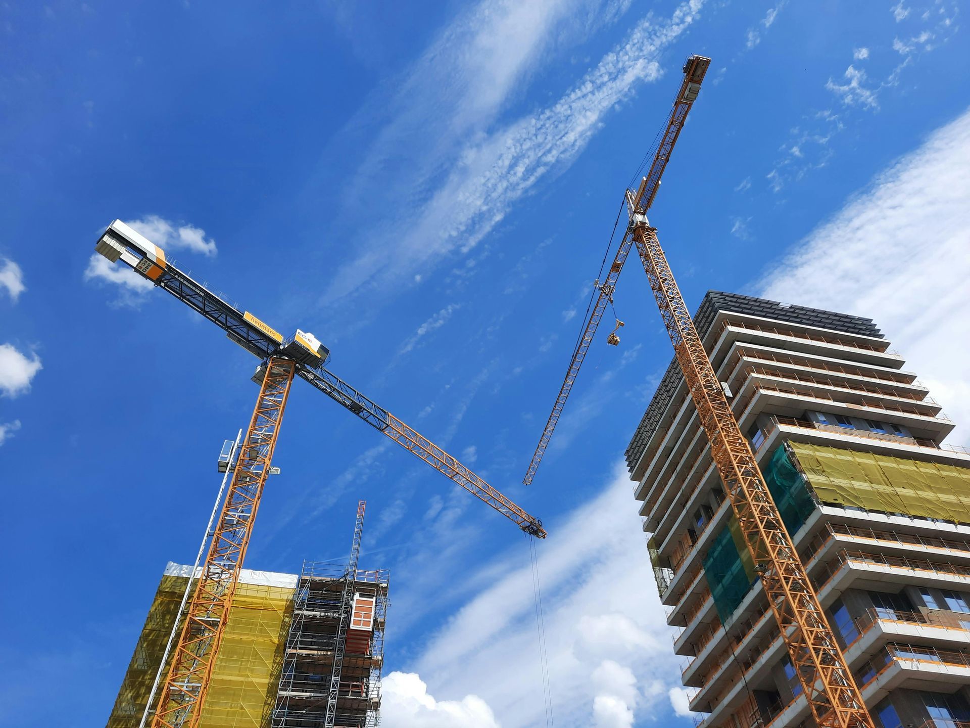Two construction cranes beside a high-rise under construction against a blue sky