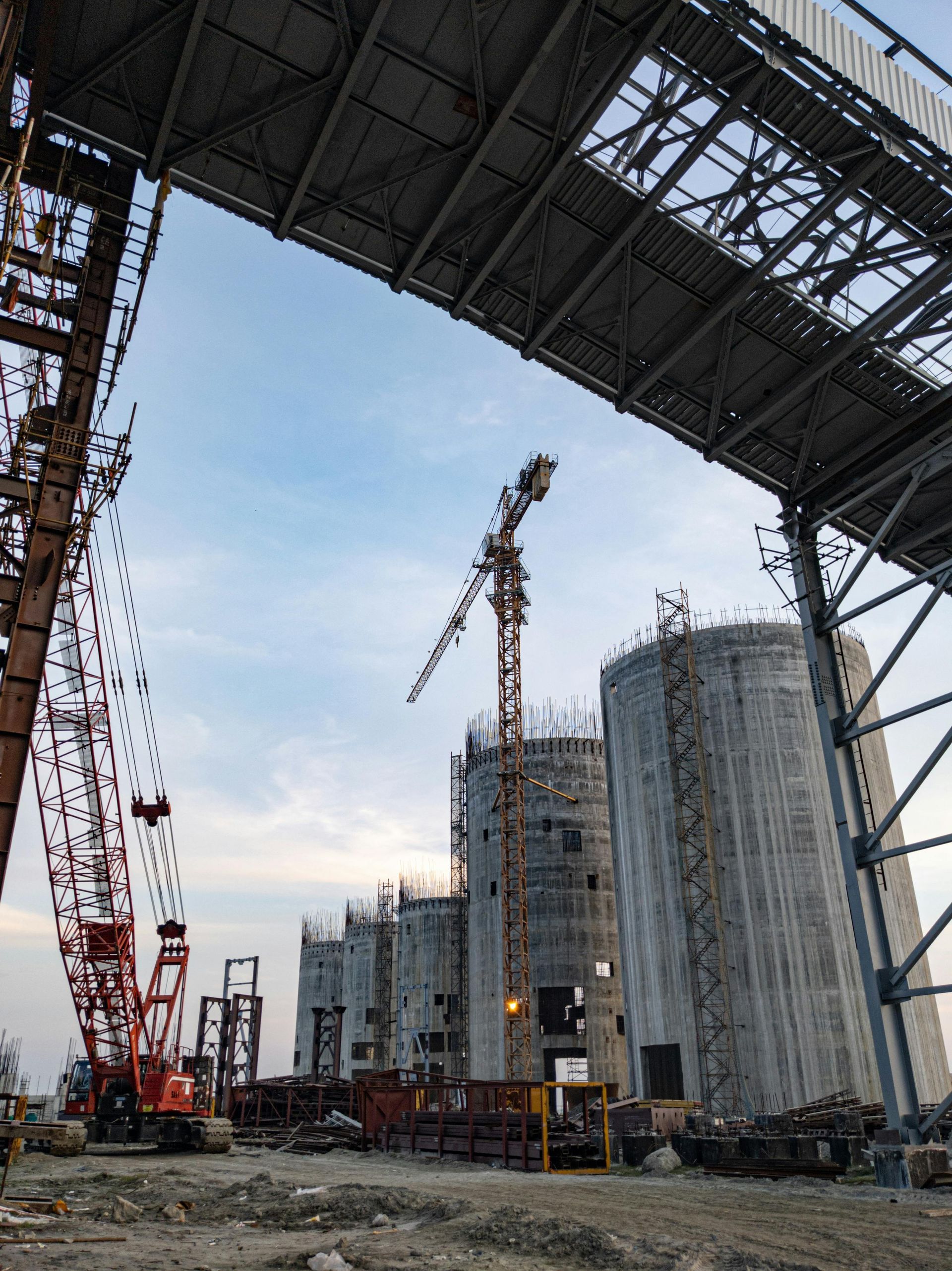 Construction site with cranes and tall concrete buildings under a steel bridge frame