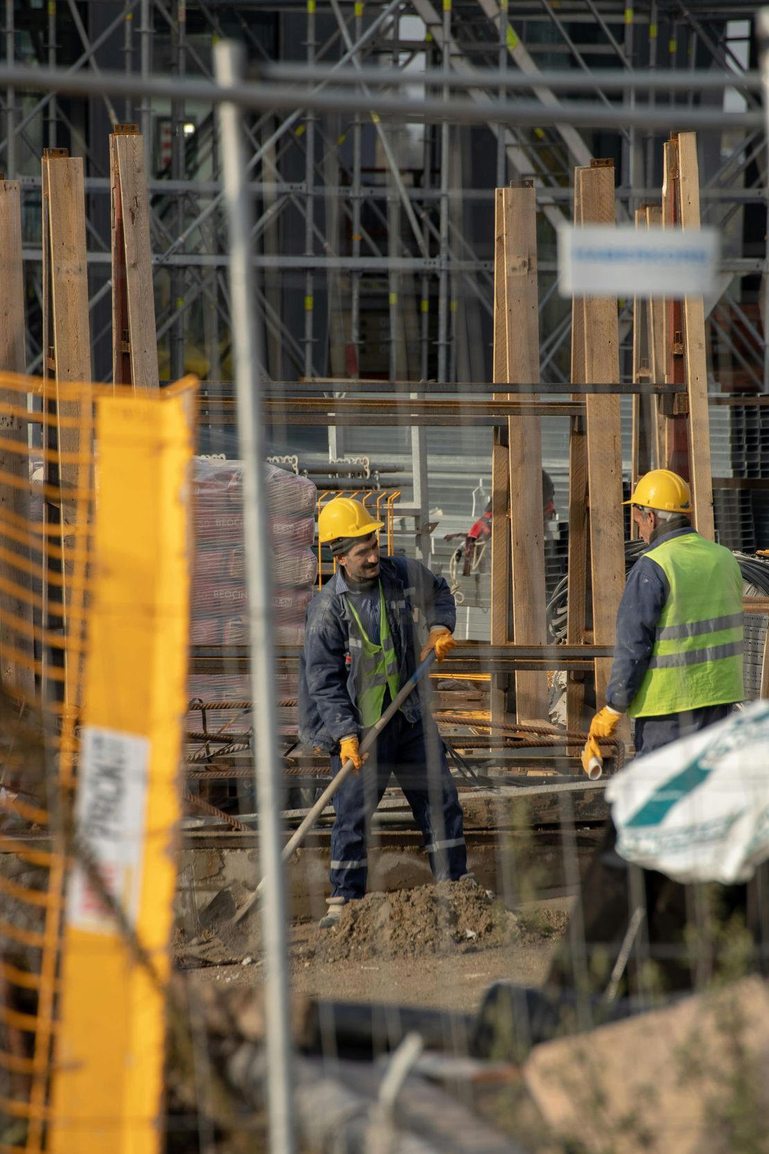 Construction workers in yellow hard hats on a building site with scaffolding and concrete columns