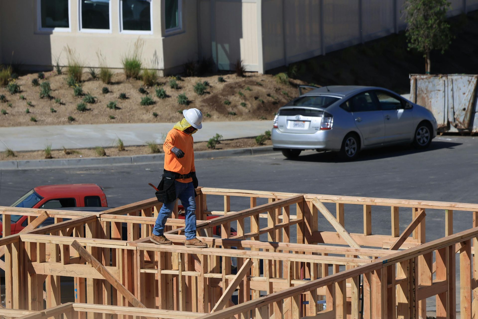 Worker in orange vest standing on wooden house framing at a construction site