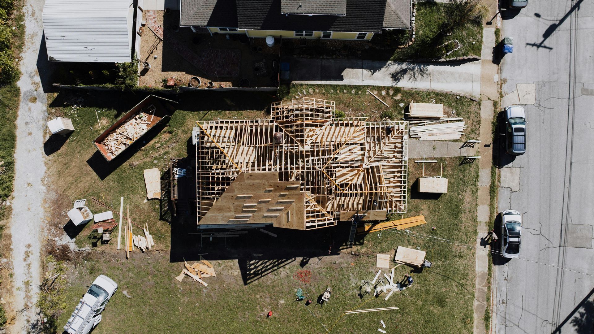 Aerial view of a house with a severely damaged roof, surrounded by debris and parked vehicles.