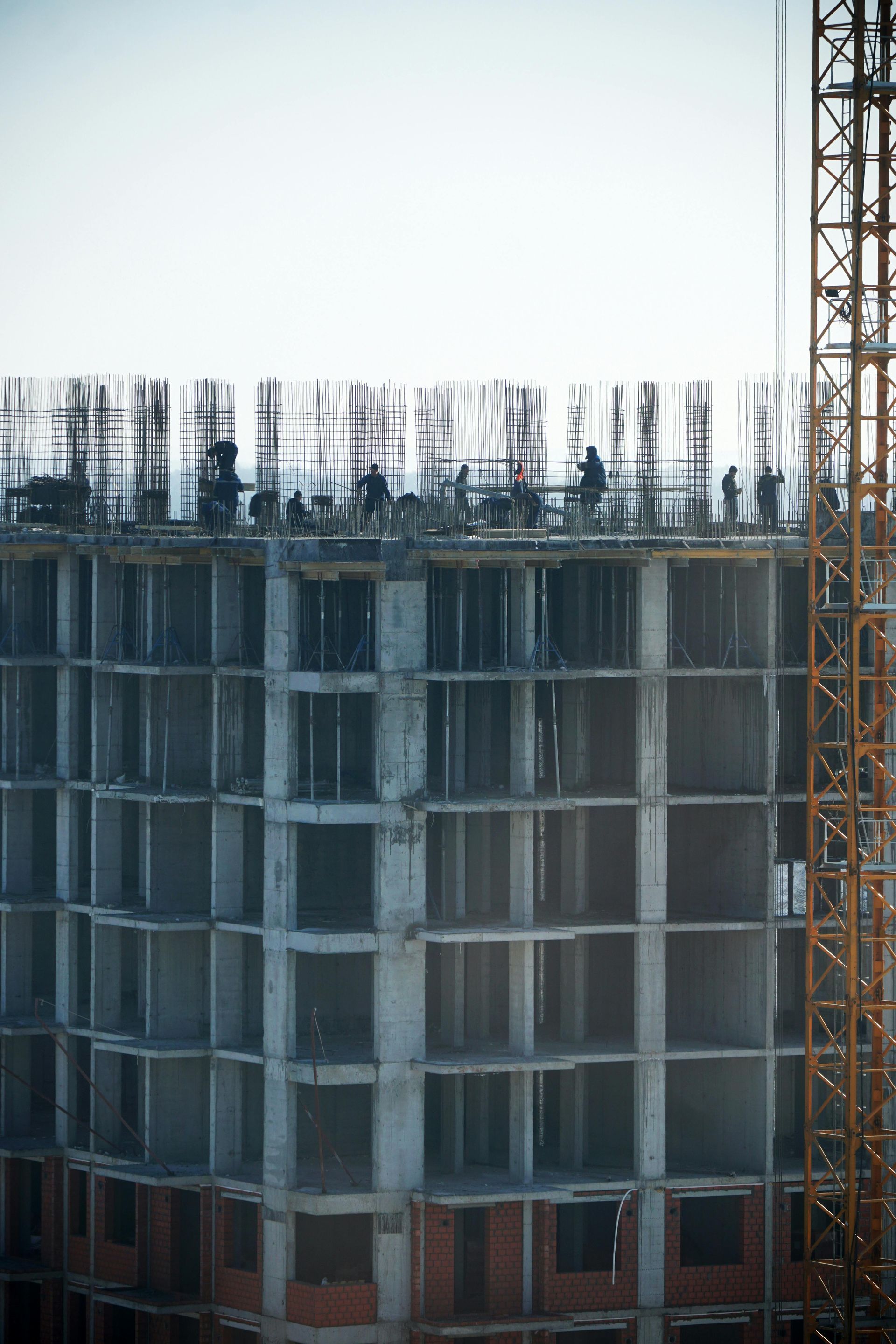 Partially built concrete high-rise with exposed rebar and a crane beside it